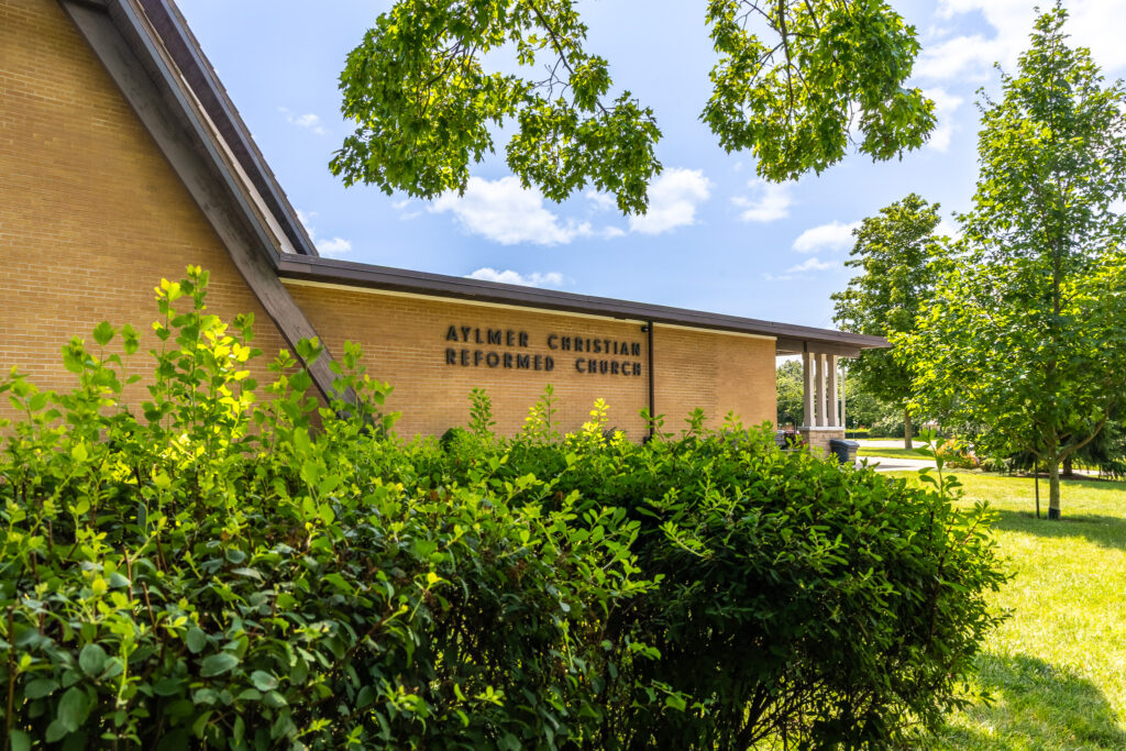 Exterior of the Aylmer Christian Reformed Church building surrounded by greenery